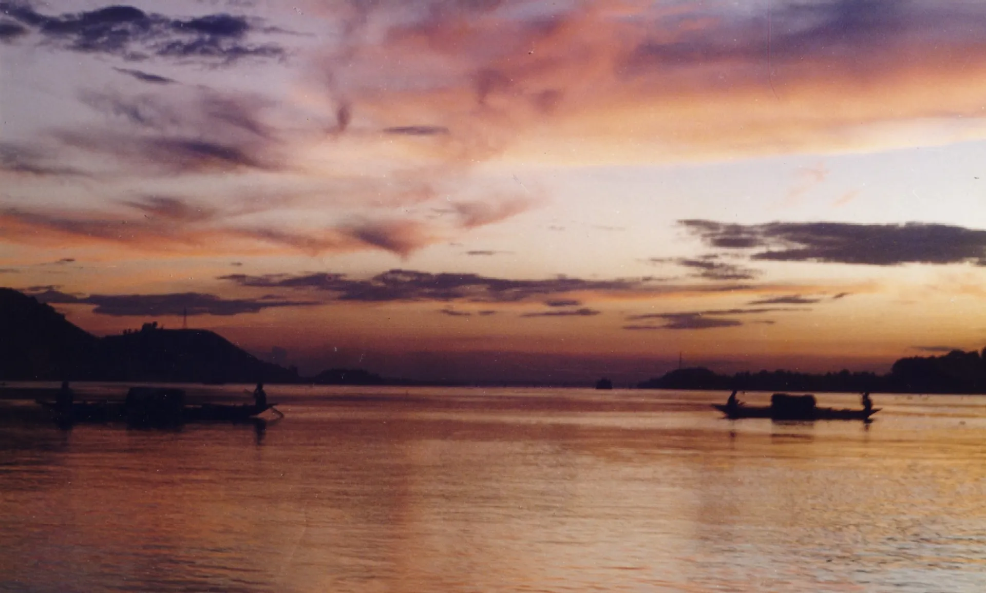 Poignant view of a sunset captured from near Sukleswar ghat in Guwahati. The photograph has a wide range of saturated colours and shows two small fishing boats and framed by the hills on both sides of the Saraighat Bridge across the river Brahmaputra. The many colours of the sky are nicely reflected on the rippling water.
